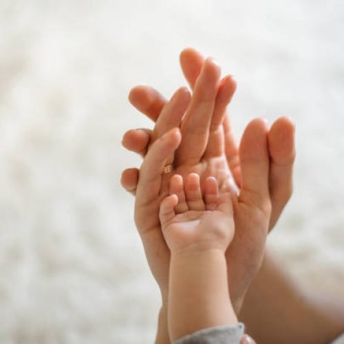 Close up of mother, father and baby join hands on the light background of room